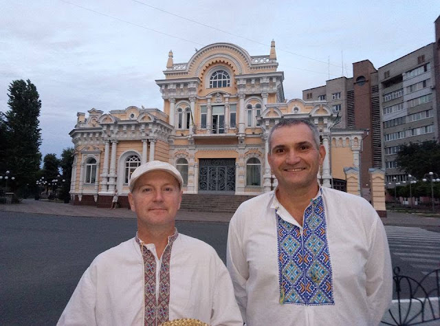 Two participants in Ukrainian embroidered shirts stand in a public square.